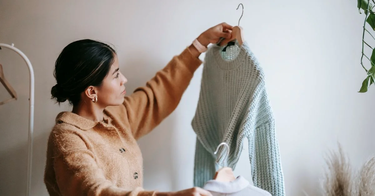 Jeune femme en tenue cozy décidant entre des pulls en tricot dans un espace intérieur.