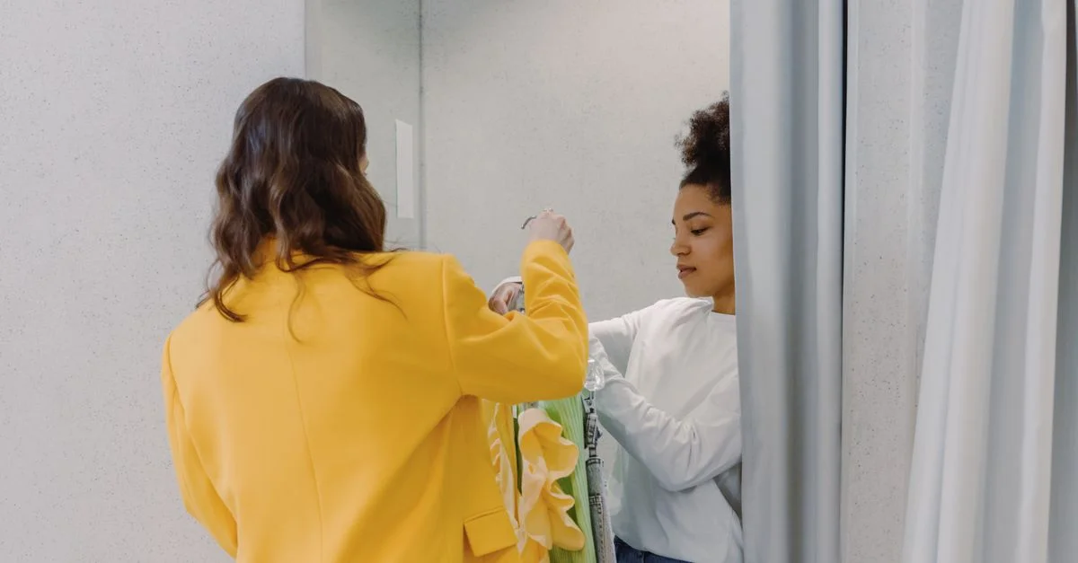 Un styliste personnel aide un client avec des choix de vêtements dans une cabine d'essayage, axé sur le style de mode.