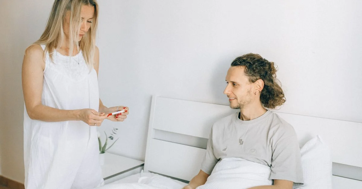 Un couple dans une chambre lumineuse partage un moment avec un test de grossesse, évoquant des émotions.