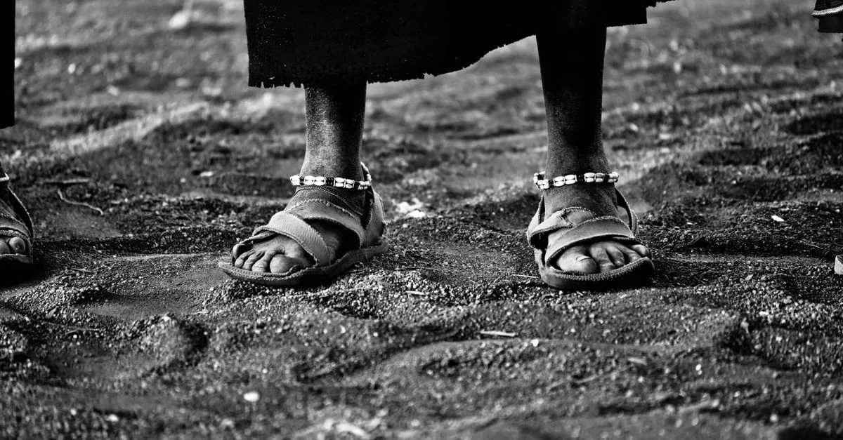 Photo artistique en noir et blanc en gros plan de pieds portant des sandales sur un sol sablonneux.
