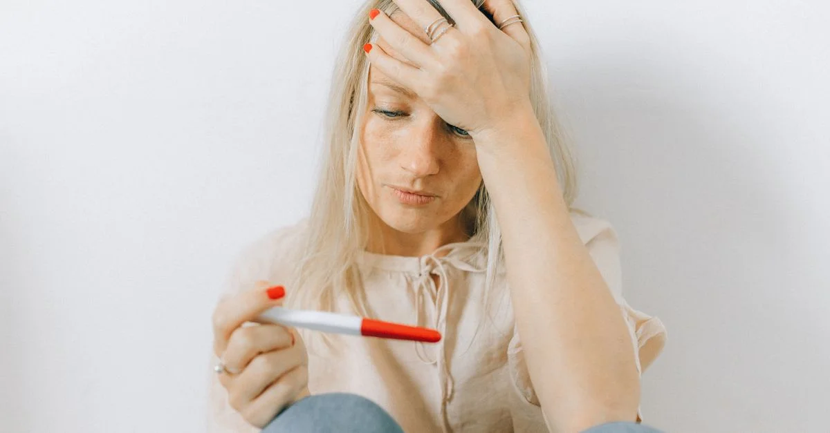 Une femme préoccupée regarde un test de grossesse, reflétant des émotions d'anxiété et d'incertitude.