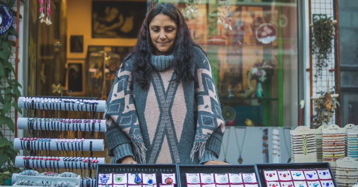 Une femme présentant des bijoux faits main dans un stand de marché de rue animé.