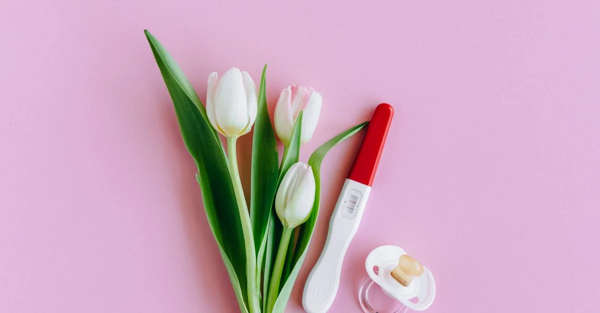 Composition de test de grossesse, tétine et tulipes sur une surface rose évoquant la fertilité et les nouveaux départs.