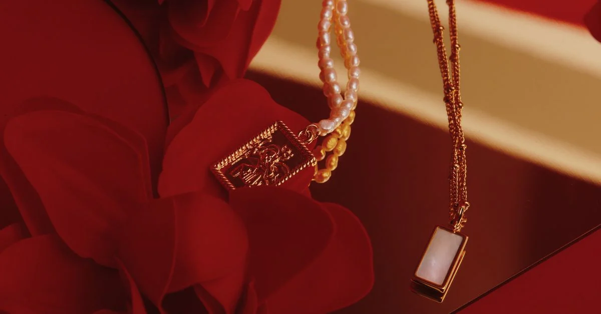 Gros plan sur des colliers en or et en perles sur un fond floral rouge, design élégant.