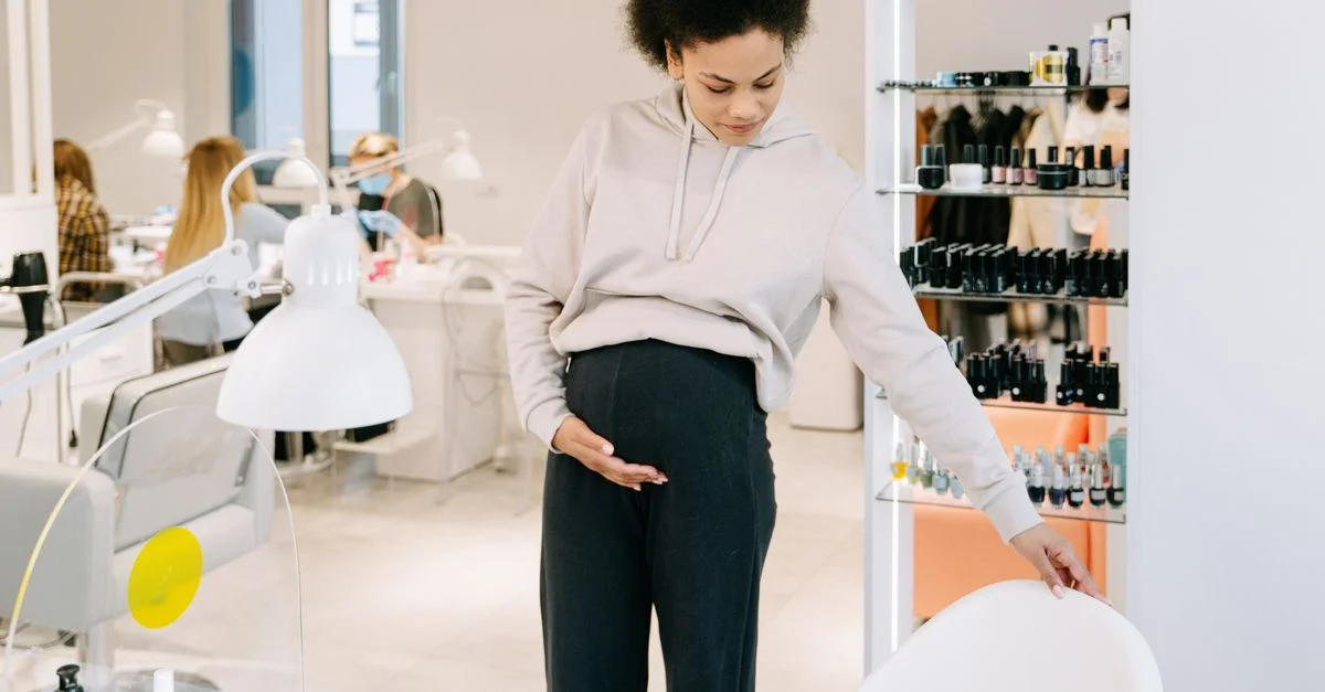 Femme enceinte avec des cheveux afro inspecte une chaise blanche dans un cadre de salon moderne.