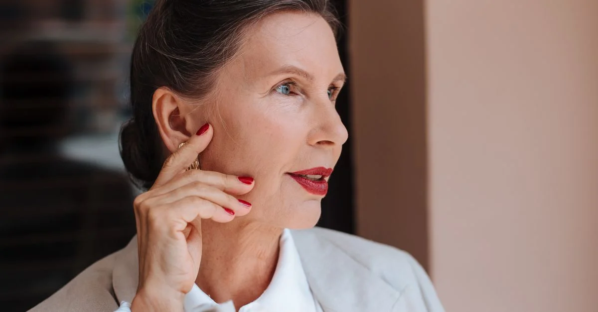 Portrait d'une élégante femme senior avec des lèvres rouges et des ongles manucurés, incarnant grâce et confiance.