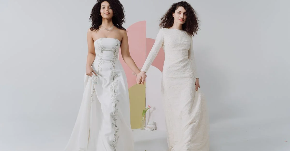 Deux demoiselles d'honneur élégantes vêtues de robes raffinées se tiennent par la main dans un studio lumineux.