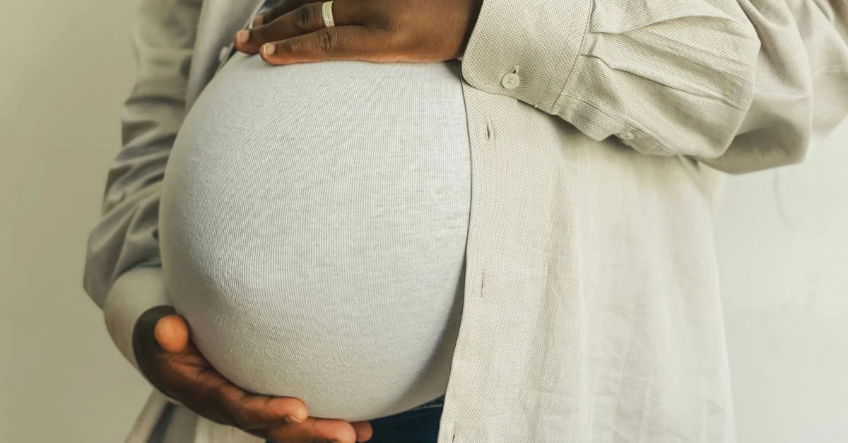 Femme enceinte en tenue décontractée tenant doucement son ventre, symbolisant la maternité.