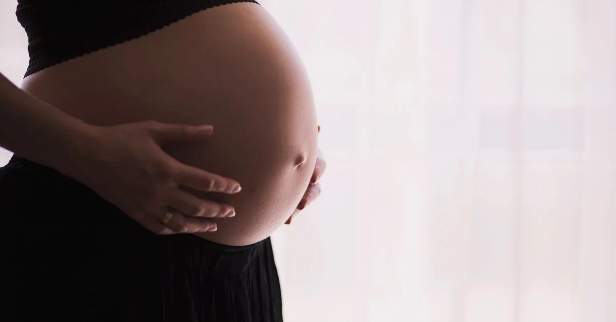 Gros plan d'une femme enceinte touchant son ventre nu, exprimant chaleur et tendresse.